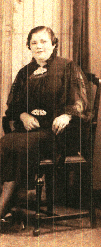 A sepia-toned portrait of a woman seated on a chair, wearing a dark, ornate dress and looking directly at the camera.