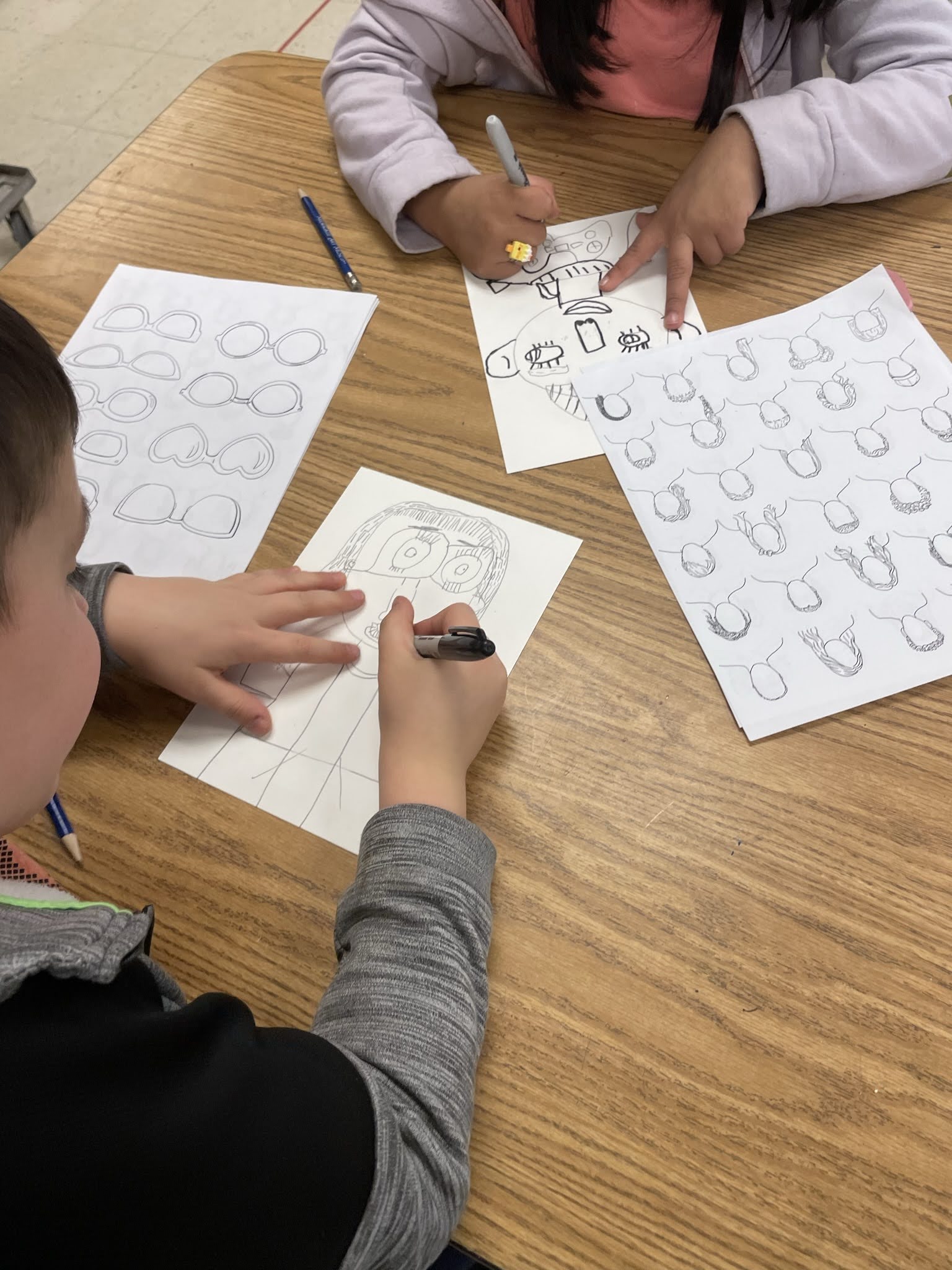 Children engaged in drawing activities at a table, with various sketches and drawings on white paper.